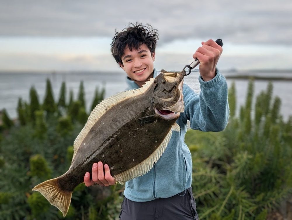 Alden holding a halibut by the water
